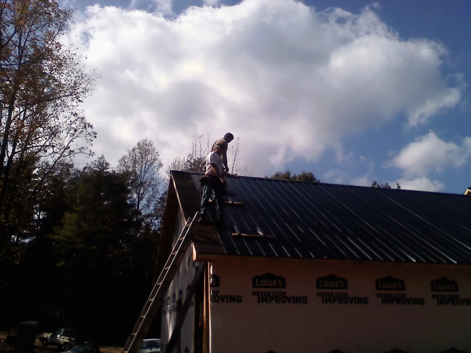 Roofer fastening dark metal panels high against a cloudy sky, from a Roof Inspection job in Bethlehem
